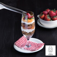 不鏽鋼材質的公筷夾，正在夾取杯中甜點裡的草莓，旁邊有裝滿草莓的白色碗。