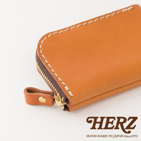 日本HERZ職人手作皮革分隔收納迷你錢包，選用棕色Stare皮革製成，錢包側面展示精緻的白色粗縫線細節與金屬拉鍊，拉鍊頭附有同色皮革扣帶，整體呈現簡約質感與日本手工藝細節。