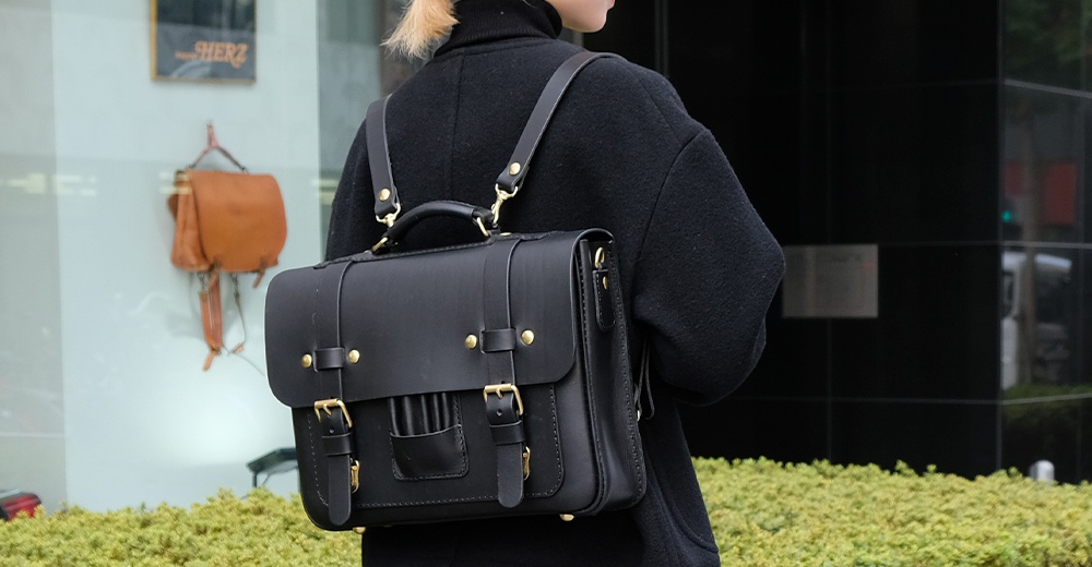 黑色皮革三用學生包，帶有金色釦環和皮帶。包款設計為傳統歐風，可後揹、側揹或手提。