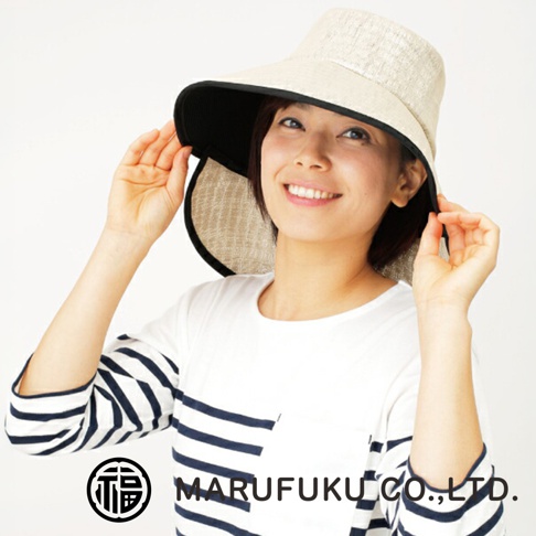 一位女性正微笑展示MARUFUKU丸福纖維的抗UV多機能遮陽寬緣帽，這款帽子外觀呈現淺米色亞麻質感，內部採用黑色隔熱素材，設計簡約且帽緣寬大，能有效遮蔽陽光。
