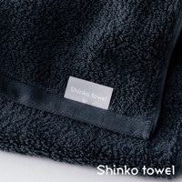 深藍色匹馬棉浴巾，帶有淺灰色標籤，標有「Shinko towel」字樣。浴巾材質柔軟，紋理細緻，呈現高品質觸感。