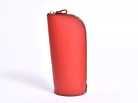 紅色皮革製成的直立式收納筆袋，側邊縫線清晰，頂部配有金色拉鍊和皮革拉環。