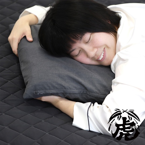 一位女性仰躺在菱格紋黑色床墊上，頭枕著一個炭灰色枕頭，枕頭布料有細緻的織紋，枕頭一側有拉鍊。