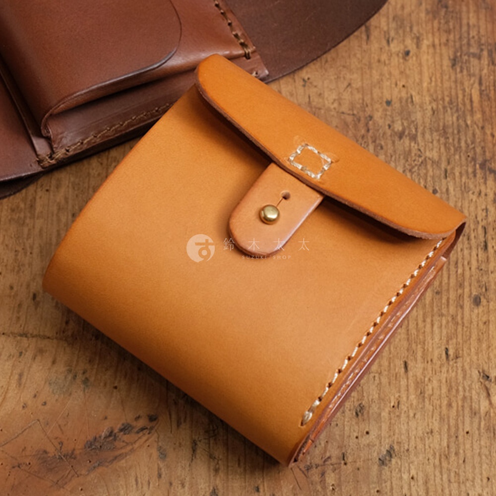 淺棕色皮革製成的職人手作二折式短夾，帶有原子釦開合設計，縫線精緻，質感溫潤。