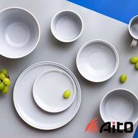 一組淺灰色美濃燒陶瓷餐具，包含不同尺寸的碗盤和杯子，擺放在灰色與藍色背景上，部分餐具裝飾有綠色葡萄。