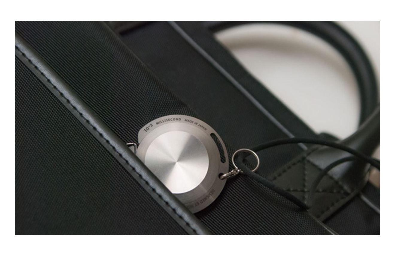 銀色鋁製圓形卷尺，附有鑰匙圈，置於黑色布質包上。卷尺表面有「10-3 MILLISECOND MADE IN JAPAN」字樣。