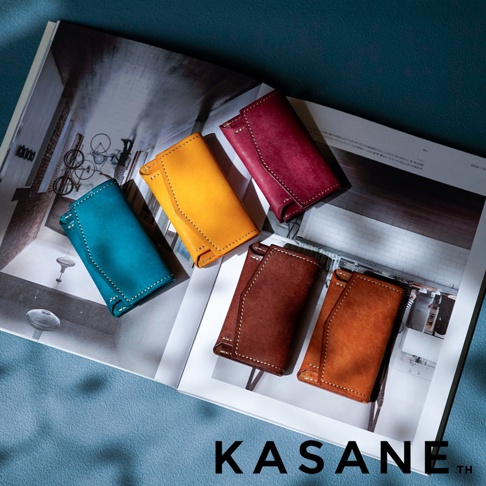 北海道KASANE品牌，職人手作義大利Margot皮革迷你雙折短夾，共五色，圖片展示有紅、黃、綠松石藍、深棕、橘棕五種顏色的短夾，擺放在一本雜誌上。
