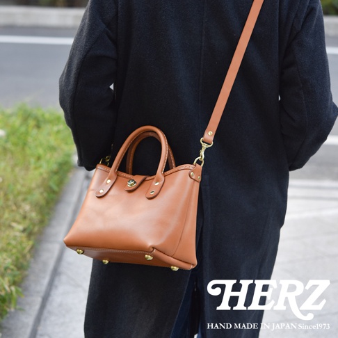 棕褐色皮革迷你托特包，配有可拆卸肩帶，包身設有頂部提把、金色金屬扣及四個底部防磨釘。