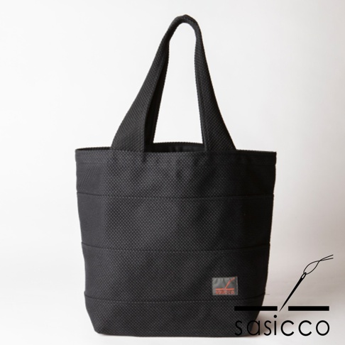 黑色三河木綿刺子織大容量托特包，織紋清晰，包身有多條橫向車縫線，左下方有一個橘色標籤。
