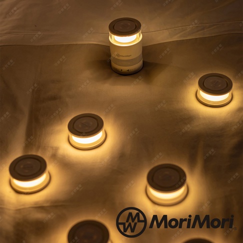 白色圓柱形音響，頂部和底部有環狀暖黃色燈光，與周圍地面上散落的幾個相同燈光的小圓形裝置一同營造氛圍。