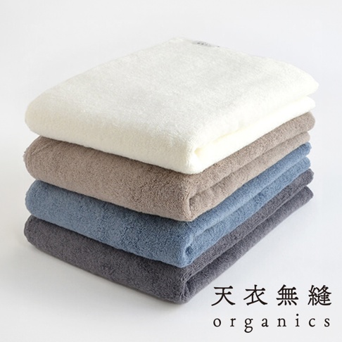 堆疊的 Lisse 蓬鬆柔感有機棉浴巾，從上至下依序為白色、淺棕色、藍色和深灰色，質地蓬鬆。