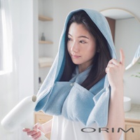 一位女性使用藍色吸水毛巾頭巾，頭巾有扣子固定，肩部包裹著毛巾，她正用吹風機吹乾頭髮。