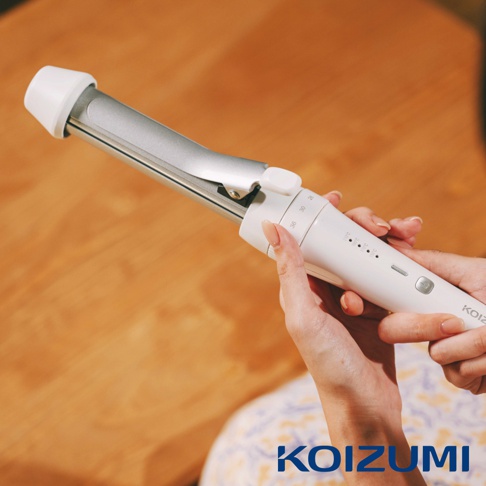 手持白色電棒捲，捲筒為銀色金屬材質，上方印有溫度刻度，下方有品牌標誌。