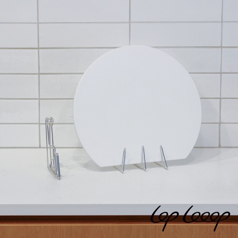 伸縮式不鏽鋼砧板架，銀色金屬材質，架上放置一個白色圓形砧板，背景為白色磁磚牆面。