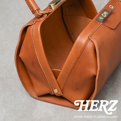 職人手作皮革Organ兩用口金手提包，採用棕褐色皮革製成，設有金屬口金開合，手提把和側面有精緻縫線，展現經典復古風格。