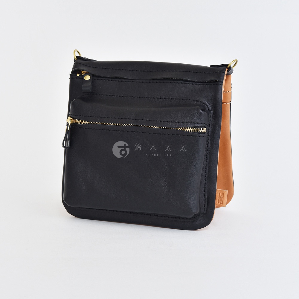 黑色皮革翻轉直式斜背包，正面有一個拉鍊口袋，搭配金色拉鍊。包包側邊為棕褐色皮革。