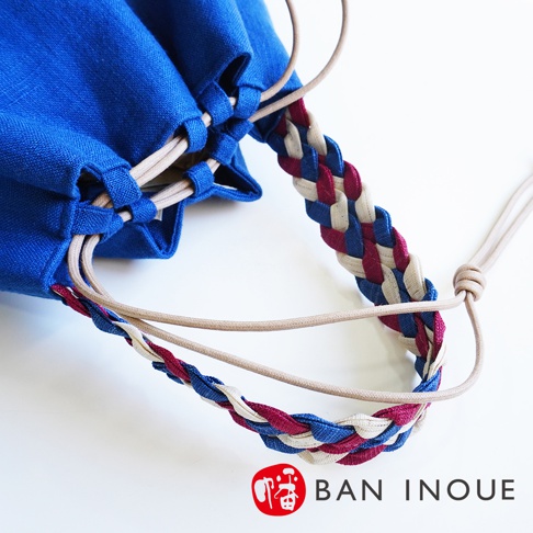 BAN INOUE 藍色束口袋手提包，搭配米色、藍色、紫紅色交織的麻花辮背帶，近拍特寫。