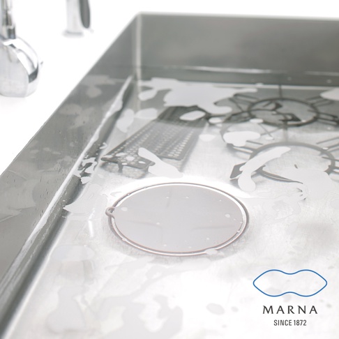 一個圓形淺灰色矽膠水槽蓋，置於濕潤的鋼製水槽中，周圍有泡沫和濾水器。