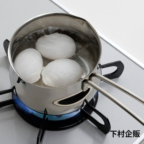 不鏽鋼牛奶鍋內煮著三個白煮蛋，鍋子放在瓦斯爐上，底部有藍色火焰。