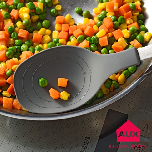 一個灰色不沾桌拌炒量匙，置於裝有豌豆、玉米粒和胡蘿蔔塊的鍋中，量匙內有刻度標示。