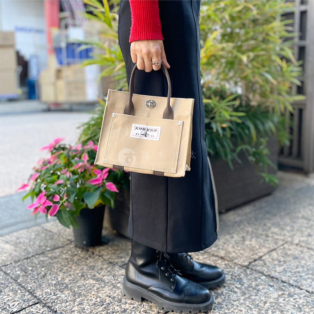 卡其色純棉帆布迷你托特包，配有深棕色提把，正面有一個貼袋，上面印有品牌標籤。
