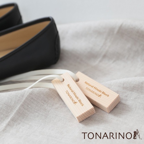 兩塊淺色天然檜木條，上面刻有「Natural Hinoki Block TONARINO」字樣，皆穿有白色細繩，置於淺灰色布料上，背景為一雙黑色皮鞋。