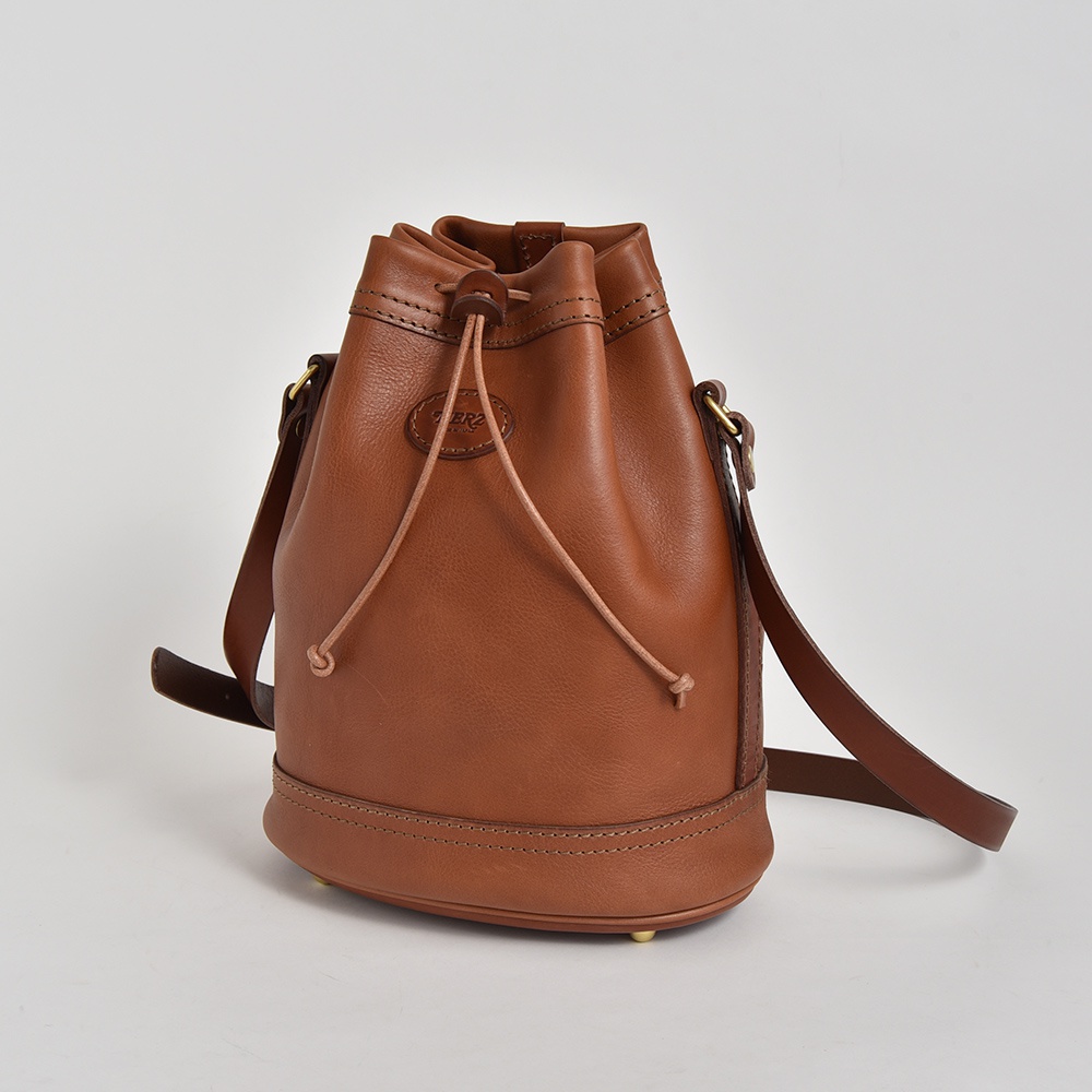 棕色皮革束口單肩包，設有抽繩開合、可調節肩帶和底部金屬腳釘，以簡潔的背景呈現。