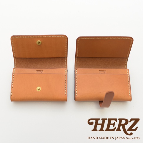 兩款日本HERZ職人手作皮革名片夾並排展示，左側款式配有金屬壓扣設計，右側款式則設有皮革插扣，皆採用淺棕色厚實植鞣革材質，搭配粗獷的米白色手工縫線，中央印有HERZ品牌標誌，整體風格簡約復古，底部標註HERZ HAND MADE IN JAPAN Since1973。