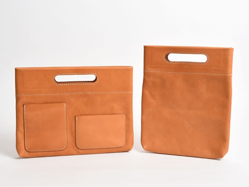 兩個棕褐色皮革製的橫式收納袋，一個有兩個外部口袋，另一個為素面，皆有頂部提把和白色縫線。