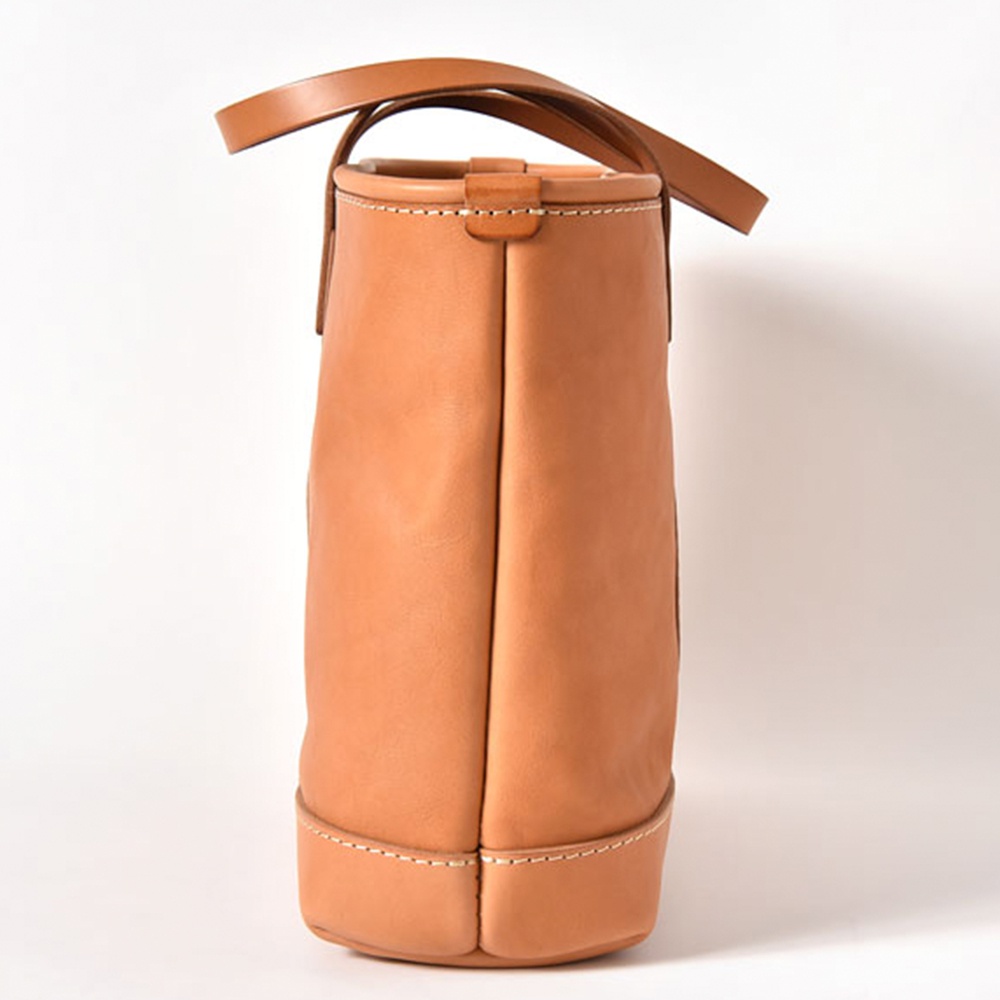淺棕色皮革手提包，圓潤的底部和頂部邊緣，配有雙提把，簡約經典的托特包設計，展現職人手作質感。