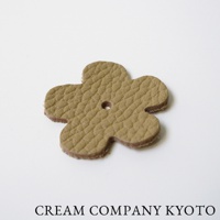 淺棕色皮革製成的四葉草造型飾品，表面有細緻的壓紋，中央有圓孔，邊緣為皮革原色。