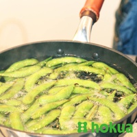 綠色毛豆在冒泡的水中翻滾，鍋子為黑色，配有木柄。