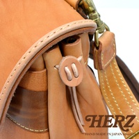 職人手作皮革鹿角扣繩郵差包，採用天然皮革材質，呈現自然的棕褐色調，包身有精緻的縫線細節，並搭配金屬旋釦與皮革綁繩開合設計。