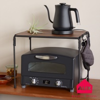 BOW 廚房工業風單層置物架，深棕色木紋檯面，黑色金屬鐵管支架，上面擺放一個黑色電熱水壺和一盆空氣鳳梨，下方放置一個黑色烤箱，右側掛有灰色隔熱手套。