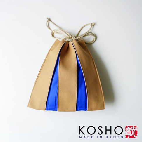 這是一款京都KOSHO品牌的ougi帆布信玄袋，採用質感帆布材質，主體呈現獨特的扇形摺疊結構，結合棕色與鮮豔藍色的撞色設計，頂部配有同色系繩結束口，整體造型簡約優雅，並在右下角印有KOSHO MADE IN KYOTO品牌標誌。