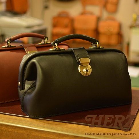 職人手作皮革長型迷你醫生包，黑色皮革包身，配有金色金屬鎖扣和提把，另一側為酒紅色皮革醫生包。