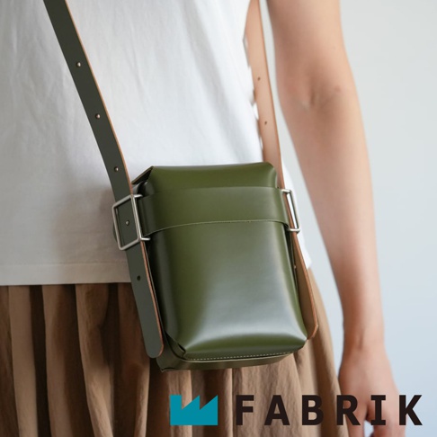 FABRIK 綠色皮革可拆式迷你斜背包，搭配棕色可調式背帶，斜背於身穿白色上衣、駝色長裙的模特兒身上