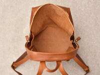 職人手作皮革後背包，呈現簡約褶皺風，主體為棕褐色，內部皮革紋理清晰可見，搭配金色拉鍊與金屬扣環。