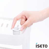 一隻手正將一個灰白色圓柱形組件插入白色三層收納架的頂部孔洞。收納架呈現淺米色，材質疑似塑膠，表面有細微顆粒。