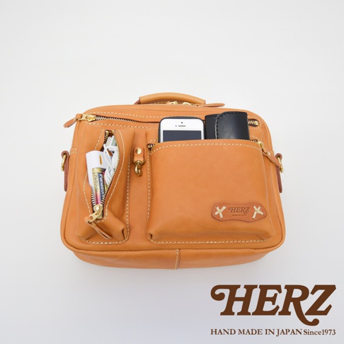 職人手作皮革兩用多功能收納單肩包，淺棕色，展示包內裝有手機、電池、充電線和卡夾，具備多個拉鍊和開放式口袋。