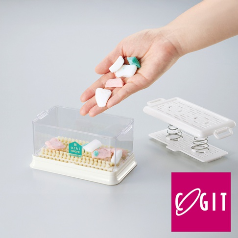 透明塑膠盒內裝有淺黃色刷毛，盒蓋上有「uchi more LAUNDRY」標誌，旁邊是一個白色帶彈簧的濾網組件，一隻手正將幾塊白色、粉紅色和綠色的洗衣皂塊放入盒中。