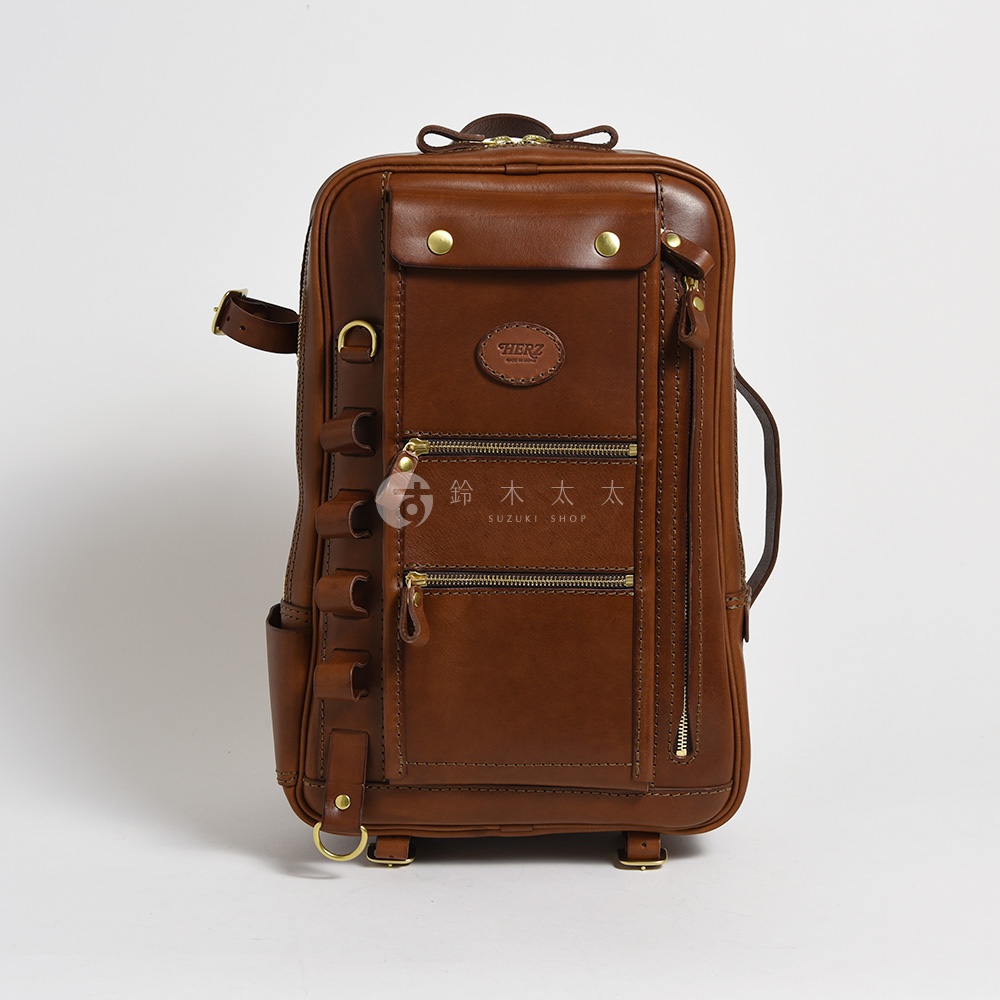 職人手作皮革兩用多功能後背包 R-66，棕褐色，結構方正，正面有多個拉鍊口袋、翻蓋口袋及品牌標誌，兩側有掛環設計，材質為真皮。