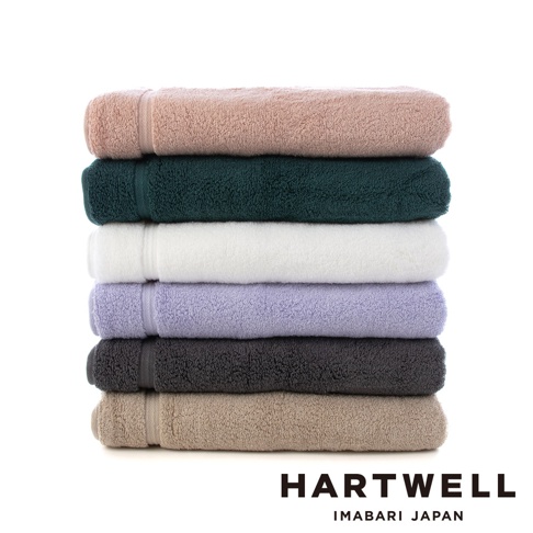 疊放的六條今治浴巾，顏色由上至下為：粉膚色、墨綠色、白色、淺紫色、炭灰色、淺褐色。浴巾質地輕盈，表面有細緻的毛圈。