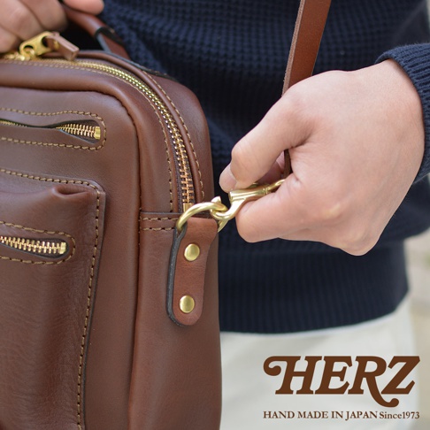 職人手作的棕色皮革單肩包，配有金色拉鍊和鉤扣，展現精緻工藝。