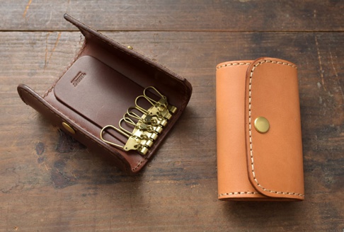 一張圖片顯示一個打開的深棕色皮革鑰匙包，內有六個金色掛鉤，以及一個關閉的淺棕色皮革鑰匙包。