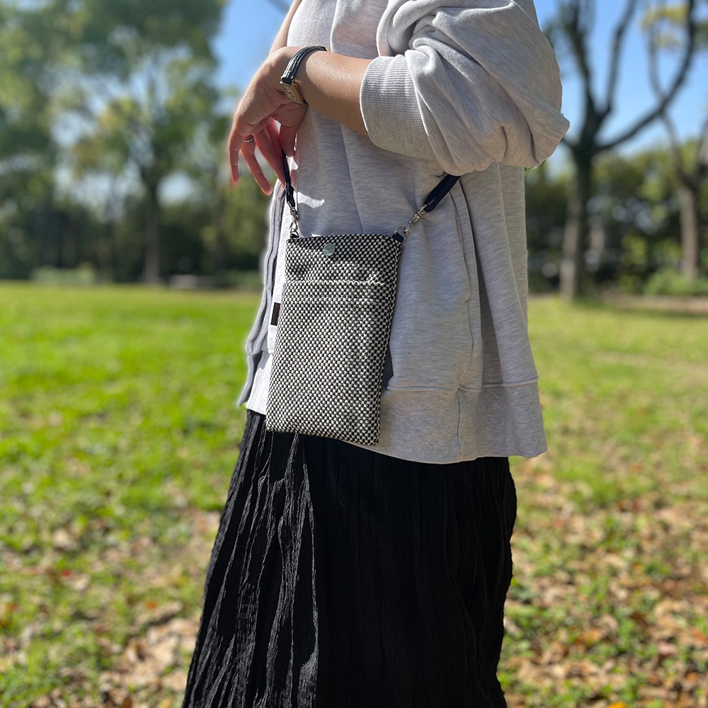 一款黑白格紋三河木綿刺子織手機包，斜掛於身，包款有兩個外袋，包蓋處有一個金屬按扣。