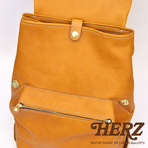 職人手作皮革多口袋後背包，呈現溫暖的橘棕色調，材質為天然皮革。包款設計有多個口袋，包含一個拉鍊前袋，並以白色車線和金色五金件點綴，展現細緻的工藝。