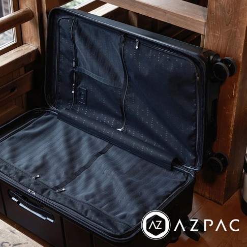 AZPAC Trucker 2.0 26吋黑色旅行箱，內部為防爆內襯，設有網狀隔層與束帶，以及品牌Logo圖案。