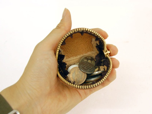 手持棕色皮革貝殼造型零錢包，內含多枚硬幣，拉鍊為金色，內裡為淺棕色皮革，邊緣有黑色裝飾。