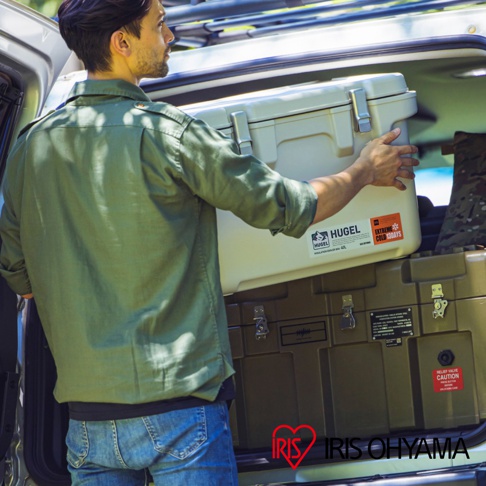 一名男子正將一個米白色、尺寸約為 20 公升的 HUGEL 真空隔熱冰桶放入汽車後座，冰桶上有「HUGEL」和「EXTREME COLD 130DAYS」的標籤。